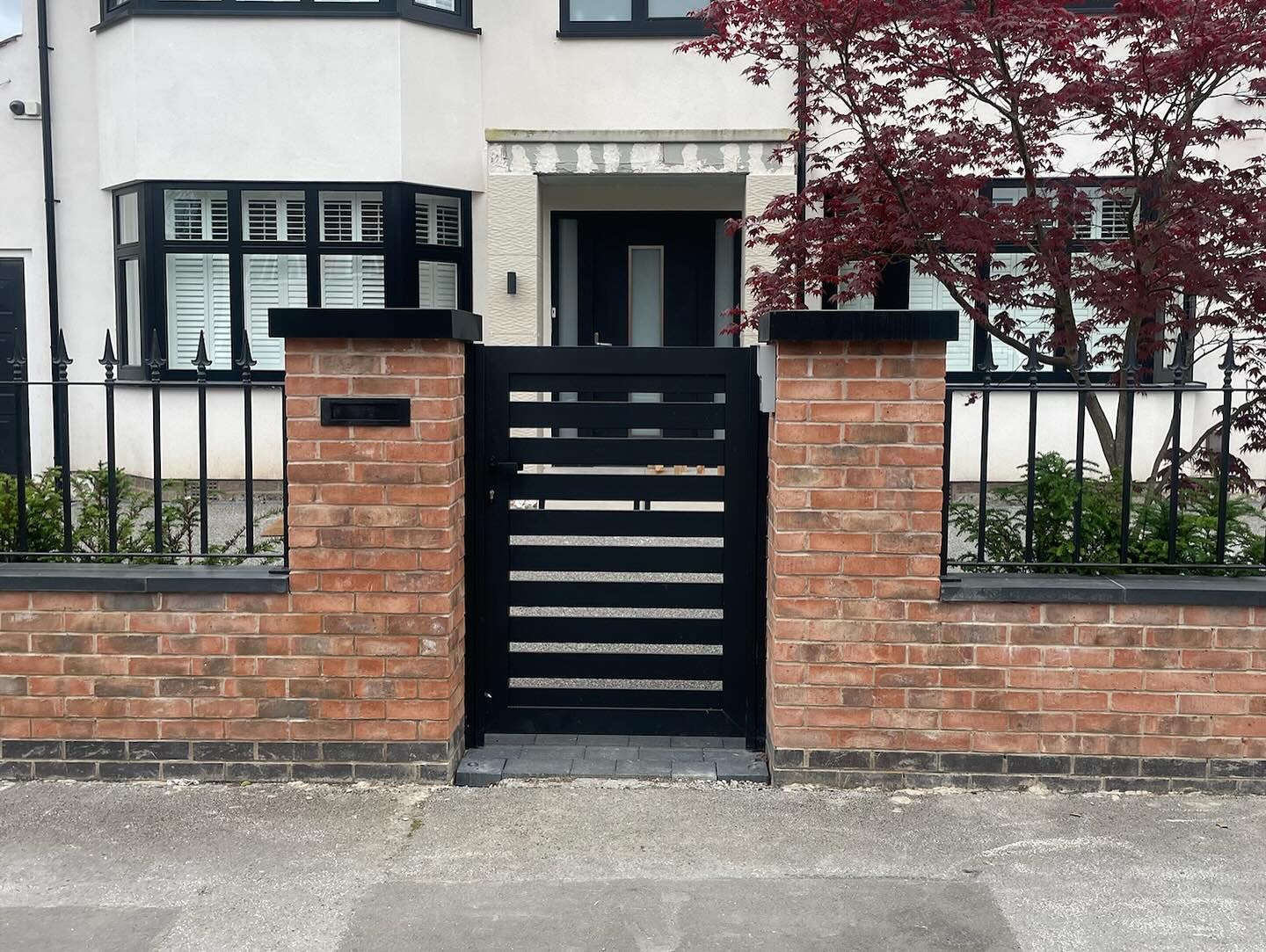 Black horizontal slatted pedestrian gate between brick pillars