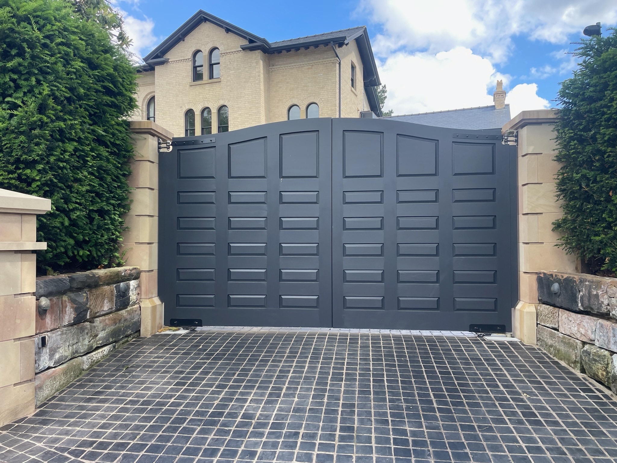 Dark grey panelled double swing gate installed between stone gateposts
